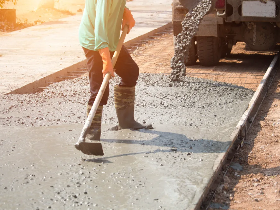 Worker raking fresh concrete level beside a mixer truck